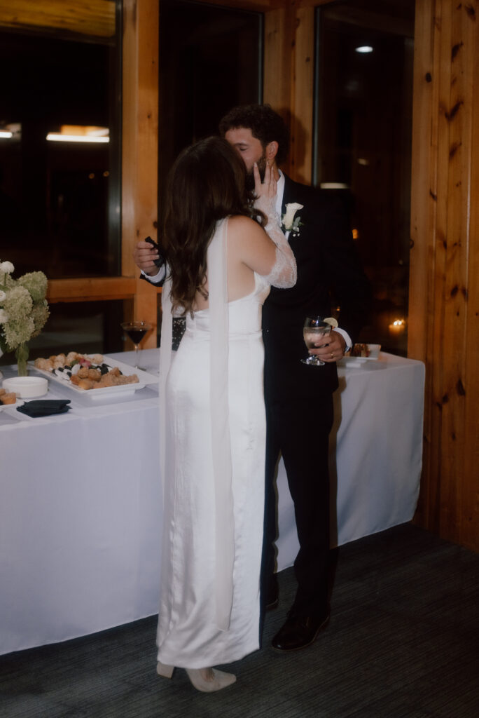 The couple shares a sweet kiss after cutting their wedding cake at HoliMont Ski Resort reception