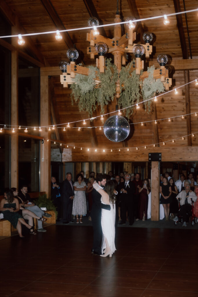 The bride and groom enjoying their first dance together under string lights at HoliMont Ski Resort wedding reception.