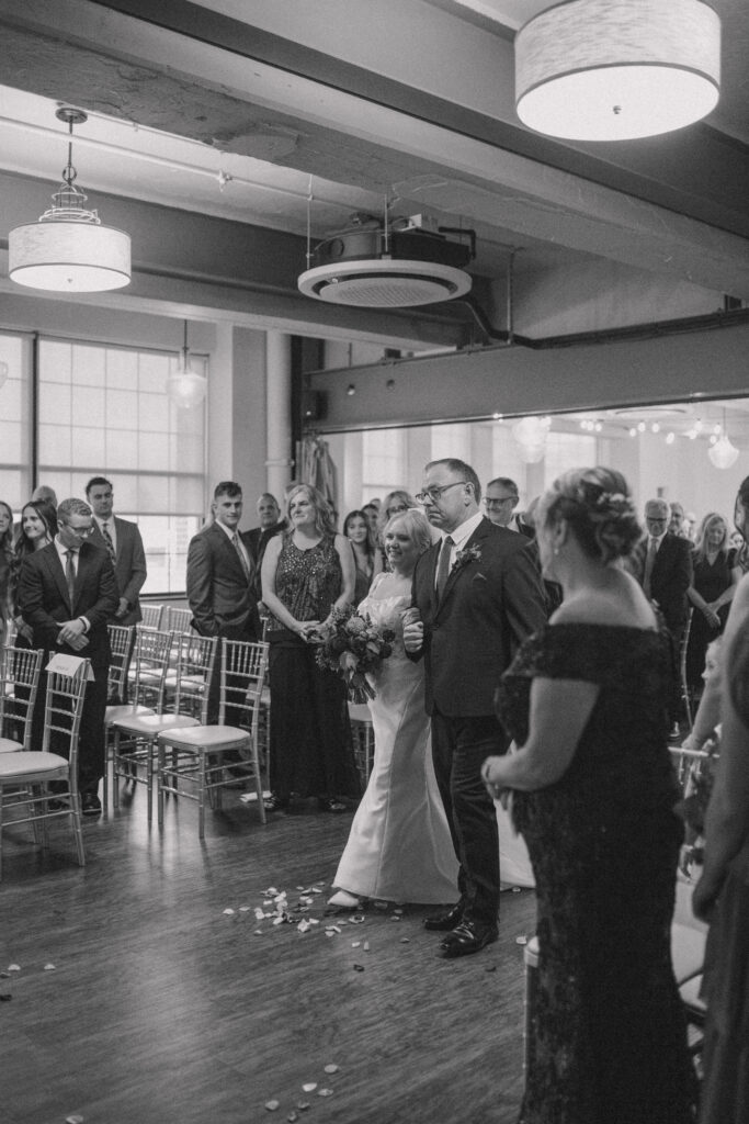 Ceremony – Megan walking down the aisle at Wurlitzer Events, smiling at Tom during the ceremony.
